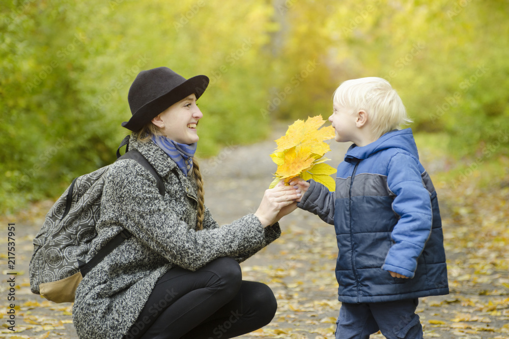 Blond boy gives his mother a bouquet of yellow leaves. Autumn forest Blond boy gives his mother a bouquet of yellow leaves. Autumn forest