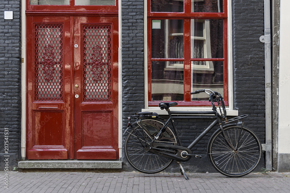A single bicycle outside a red door in Amsterdam, Netherlands A single bicycle outside a red door in Amsterdam, Netherlands