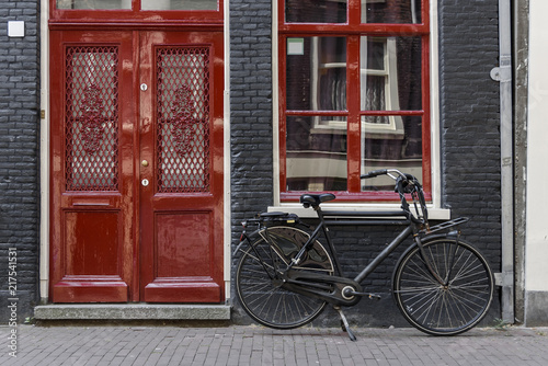 Photography A single bicycle outside a red door in Amsterdam, Netherlands