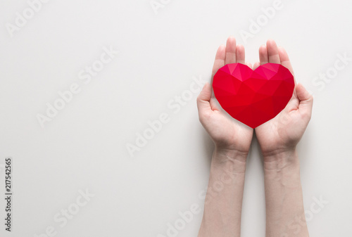 Red polygonal heart in female hands on white background. Symbol of charity and donation. Place for text.
