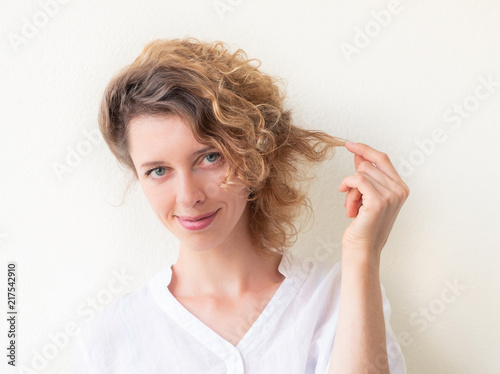 Smiling young woman holding strand of her curly hair photo