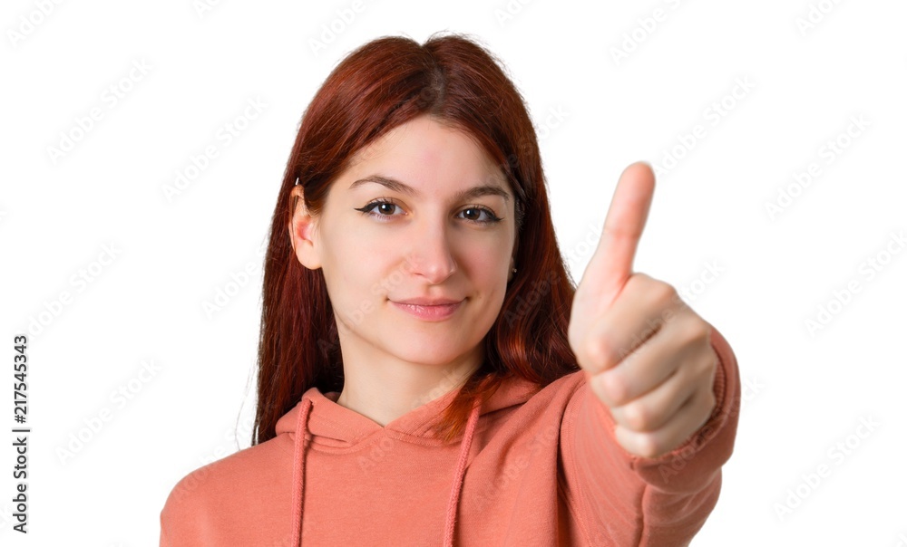 Young redhead girl with pink sweatshirt giving a thumbs up gesture and smiling because something good has happened on isolated white background