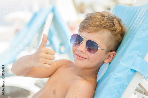the boy on a sunny beach lies on a sun lounger in sunglasses and showing thumbs up photo