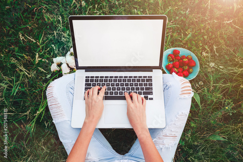 Young woman using and typing laptop computer in summer grass. Freelancer working in outdoor park.