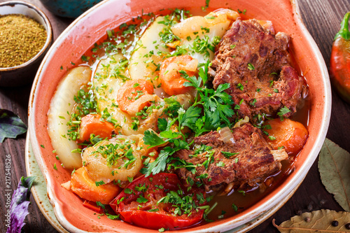 Baked meat with grilled vegetables, potatoes, greens in plate on wooden background. Hot Meat Dishes