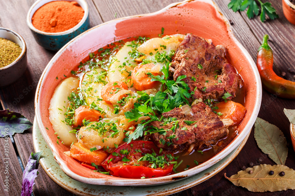 Baked meat with grilled vegetables, potatoes, greens in plate on wooden background. Hot Meat Dishes Baked meat with grilled vegetables, potatoes, greens in plate on wooden background. Hot Meat Dishes