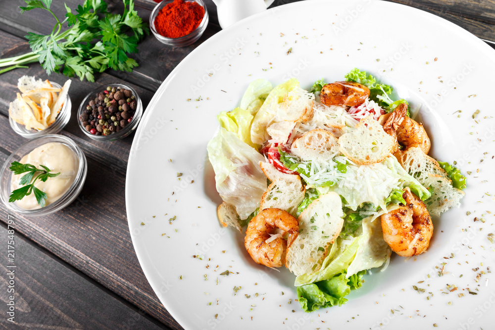 Shrimp salad with parmesan cheese, croutons, tomatoes, mixed greens, lettuce on wooden background. Healthy food