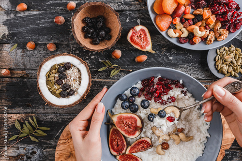 Woman eating Rice coconut porridge with figs, berries, nuts and coconut milk in plate on rustic wooden background