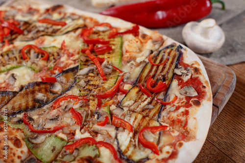 Delicious pizza with chicken, zucchini, eggplant, pepper, cheese and mushrooms on wooden rustic table. Top view. Toning