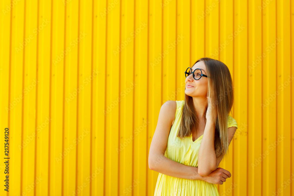 Obraz premium Portrait of a thoughtful girl wearing glasses looking up over yellow background