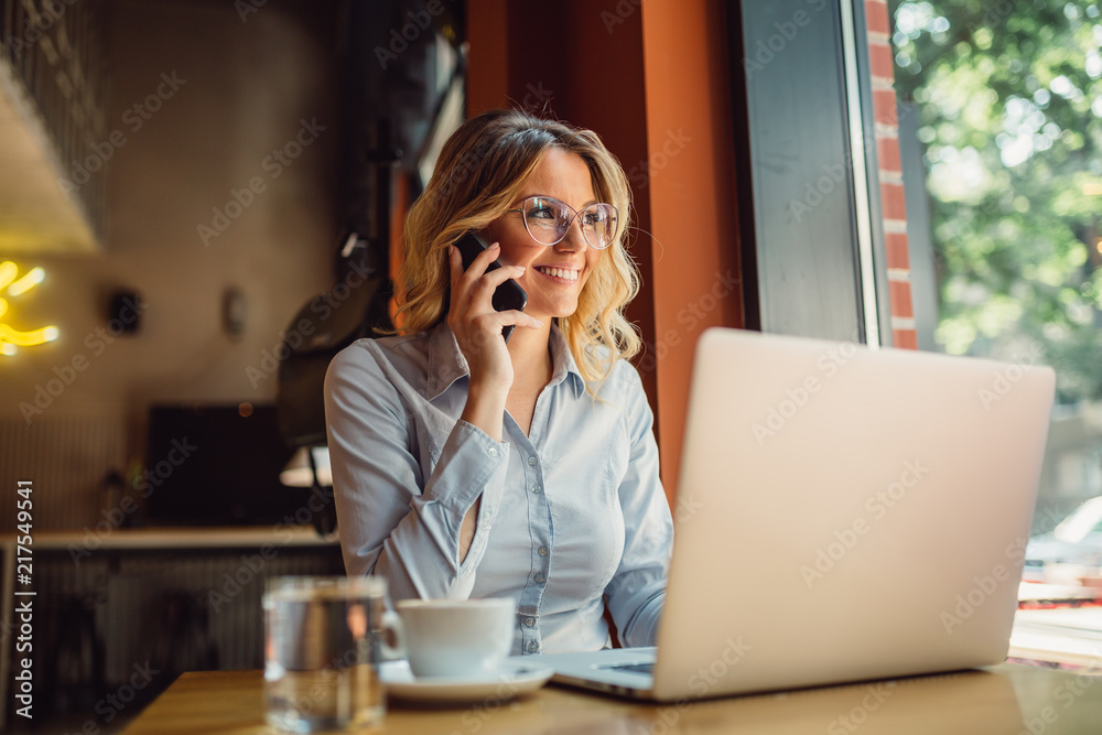© Nebojsa - Portrait of young business woman with glasses sitting in cafe in front of her laptop and talking on mobile phone © Nebojsa - Portrait of young business woman with glasses sitting in cafe in front of her laptop and talking on mobile phone