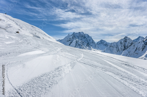 Ski slope with Mt. Dombay-Ulgen on the horizon in winter sunny day. Dombai ski resort, Western Caucasus, Russia.