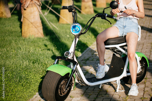 Healthy and active lifestyle. Close up female cycle-traveler legs resting on electrical bicycle on urban park lane in morning after long ride, photo