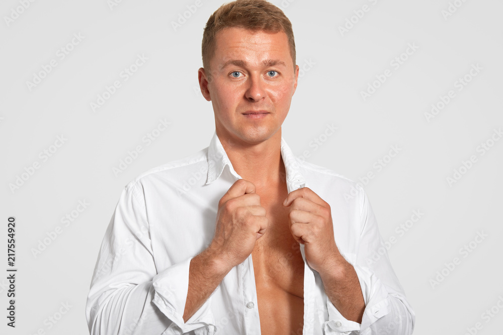 Horizontal shot of serious attractive man wears white shirt, shows his perfect body, keeps fit, being professional sportsman, has healthy skin, isolated over white background. People and sport concept Horizontal shot of serious attractive man wears white shirt, shows his perfect body, keeps fit, being professional sportsman, has healthy skin, isolated over white background. People and sport concept