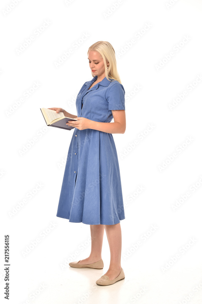 full length portrait of blonde girl wearing blue dress. standing pose holding a book. isolated on white studio background. full length portrait of blonde girl wearing blue dress. standing pose holding a book. isolated on white studio background.