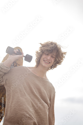 Hipster man dressed shirt, holding skateboard on shoulder, outdoor street portrait photo