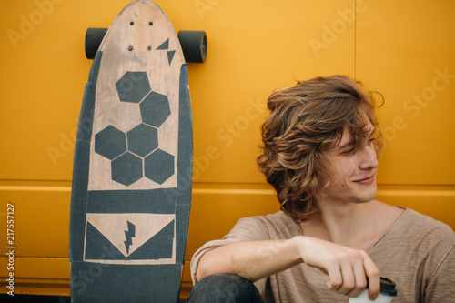man drinking coffee after riding on longboard near yellow car photo