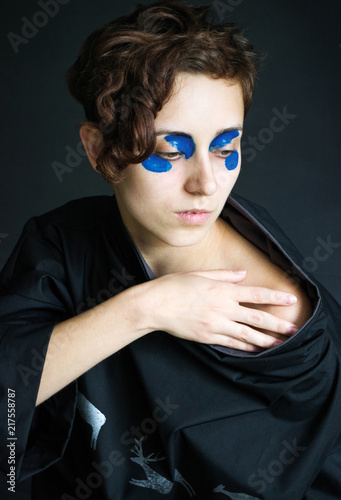 fashion photo girl with short curly hair in black clothes with a wide collar with blue paint on her eyes a hand on her shoulder