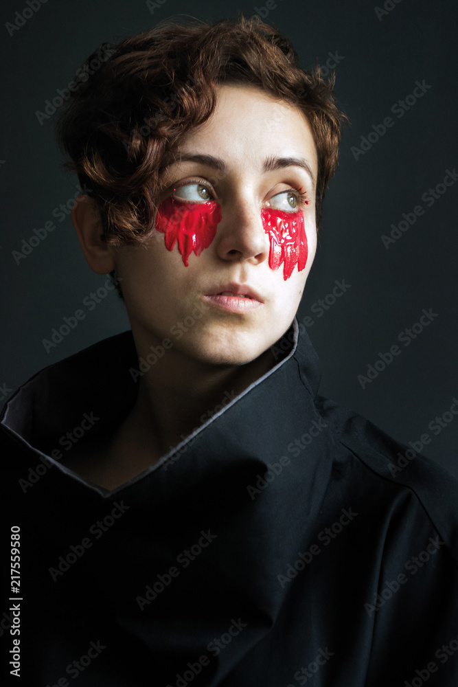 photo fashion portrait of a girl with short curly hair in black clothes with a high collar with red paint under her eyes photo fashion portrait of a girl with short curly hair in black clothes with a high collar with red paint under her eyes