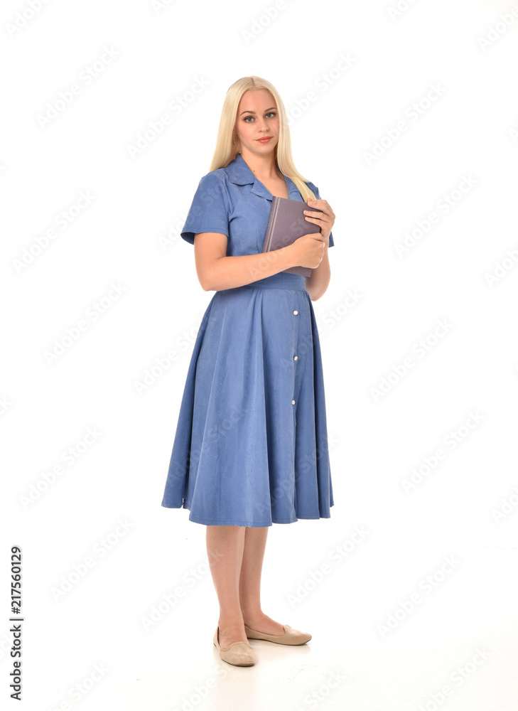 full length portrait of blonde girl wearing blue dress. standing pose holding a book. isolated on white studio background. full length portrait of blonde girl wearing blue dress. standing pose holding a book. isolated on white studio background.