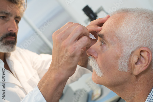 optometrist putting eye drops in senior patients eye