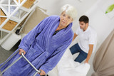 male nurse making bed while female senior using walker