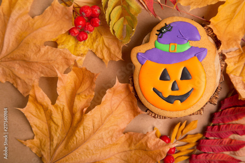 Fototapeta Naklejka Na Ścianę i Meble -  Halloween holiday - traditional sweets. Gingerbread pumpkin with a smile on the background of autumn leaves and kraft paper. Background image for inserting text.