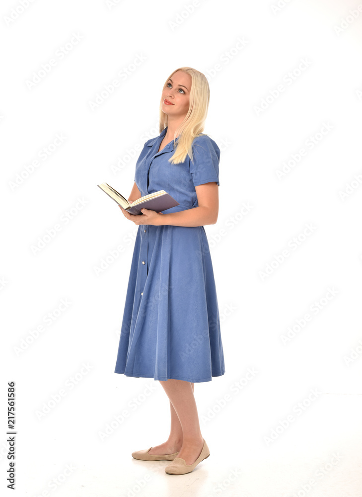 full length portrait of blonde girl wearing blue dress. standing pose holding a book. isolated on white studio background. full length portrait of blonde girl wearing blue dress. standing pose holding a book. isolated on white studio background.