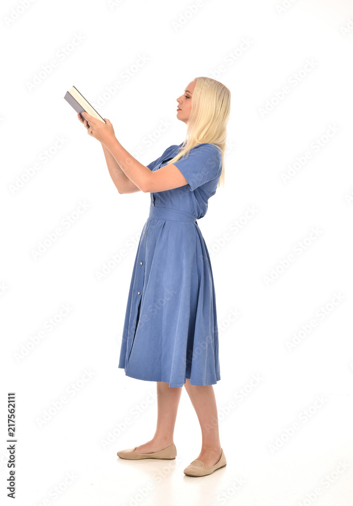 full length portrait of blonde girl wearing blue dress. standing pose holding a book. isolated on white studio background. full length portrait of blonde girl wearing blue dress. standing pose holding a book. isolated on white studio background.