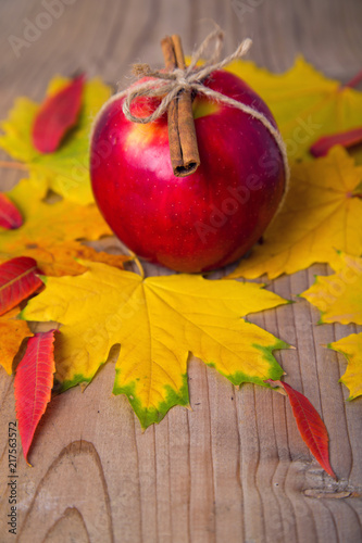Red apple with cinnamon lies on a wooden table with autumn leaves.