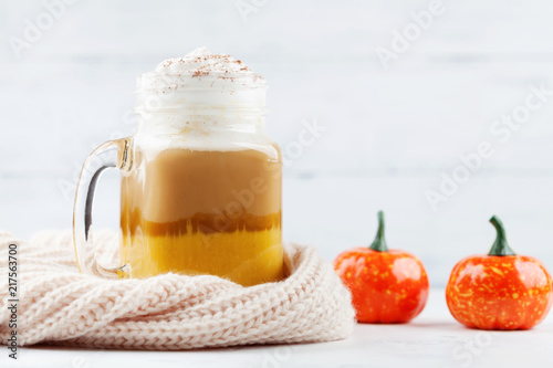 Pumpkin spiced latte or coffee in glass jar decorated knitted scarf on white table. Autumn, fall or winter hot drink.