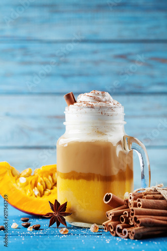 Pumpkin spiced latte or coffee in glass jar on turquoise wooden table. Autumn, fall or winter hot drink.