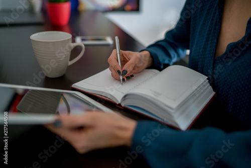 Selective focus on paper notepad, beautiful women's hands holding modern touch pad and writing planned tasks. Cropped view of female student reading useful material in network while learning by self
