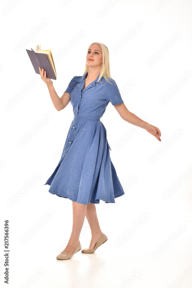 full length portrait of blonde girl wearing blue dress. standing pose holding a book. isolated on white studio background. full length portrait of blonde girl wearing blue dress. standing pose holding a book. isolated on white studio background.