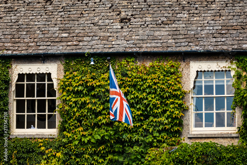 Medieval Cotswold stone cottage with British flag between windows in the village of Bibury, England