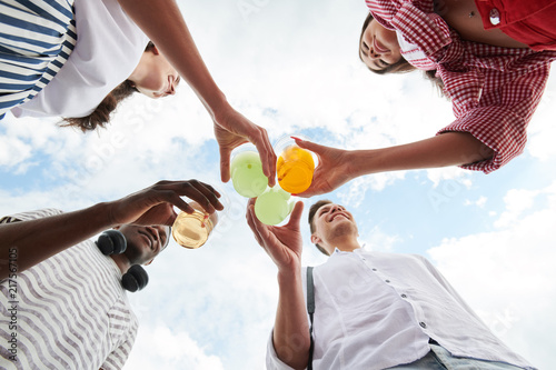 Low angle view of young smiling people toasting with cold cocktails in summer day
