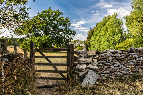 Wooden gate and stone wall along farmland, Cotswolds, England
