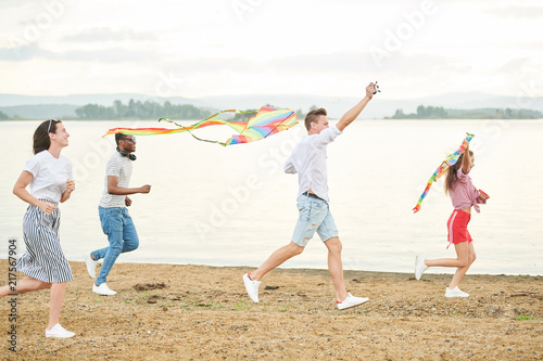 Group of friends running on the beach with flying kites