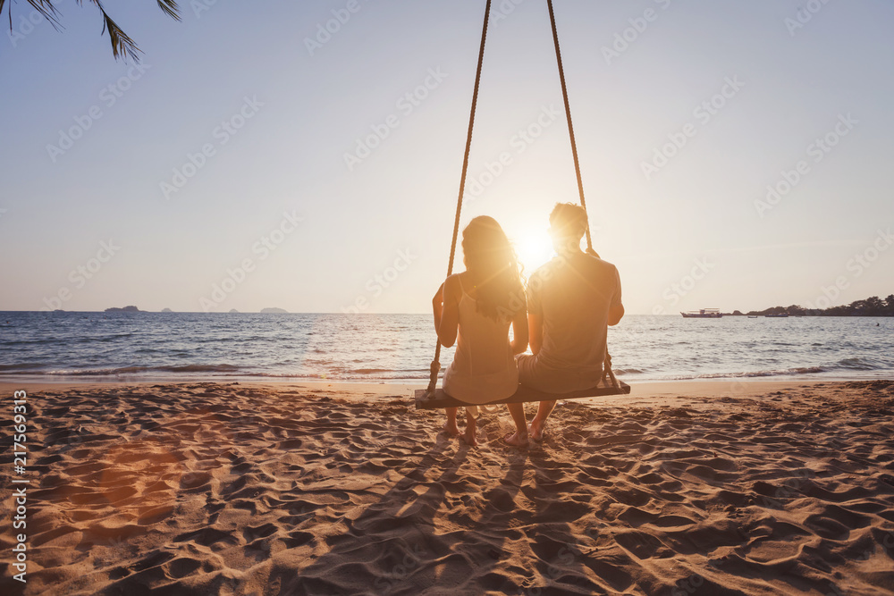 beach holidays for romantic young couple, honeymoon vacations, silhouettes of man and woman sitting together on swing and enjoying sunset - obrazy, fototapety, plakaty 