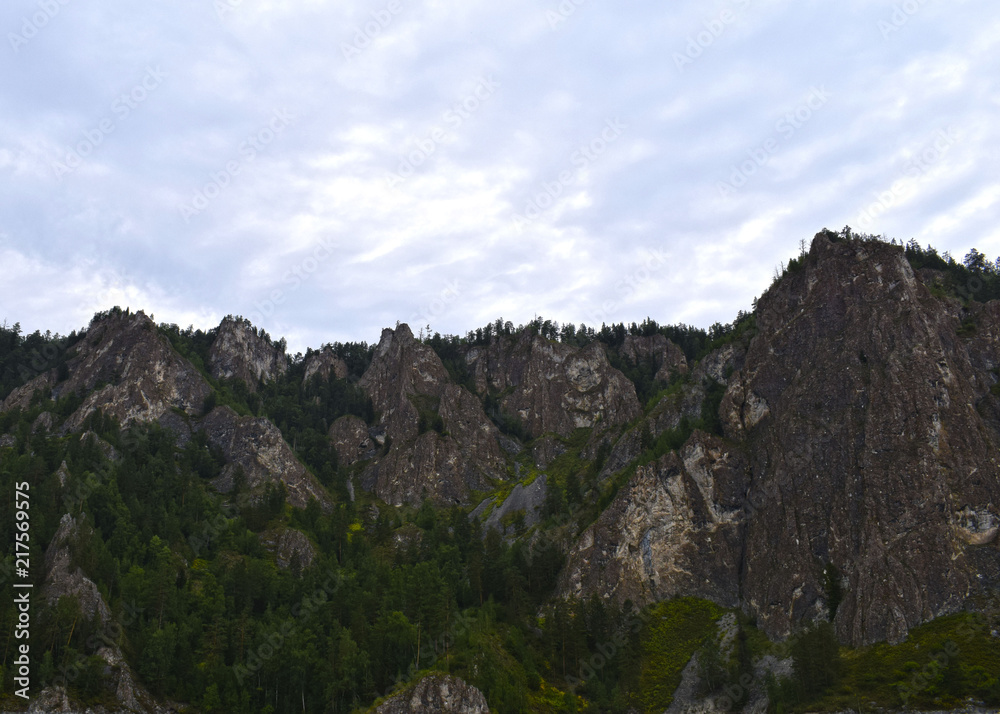 Picturesque view of the rocks surrounded by forest. Speleology. Rocky shore. High mountains against the sky. Mountaineering.