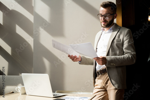 Confident executive standing at office and examining business contract before meeting photo