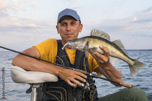 Happy fisherman with zander fish trophy at the boat with fishing tackles