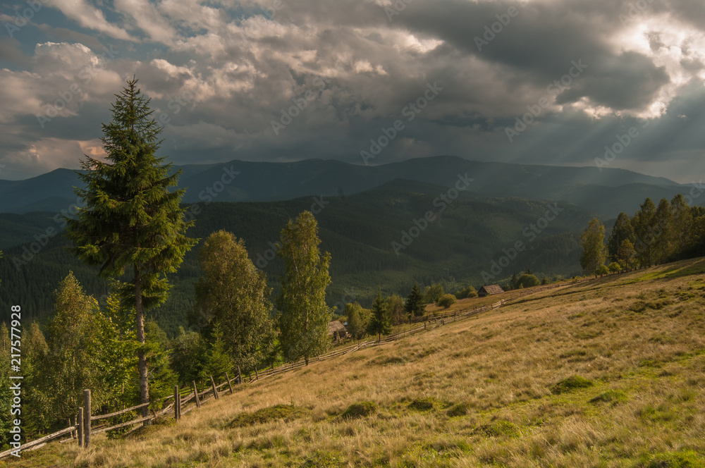 Carpathian mountains meadow, sun rays under the hills, clouds