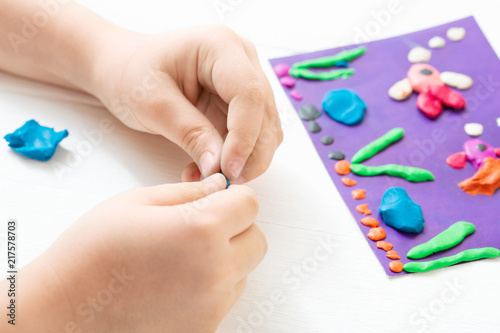 A child kneads plasticine and sculpts an aquarium with fish. Tutoring with children photo