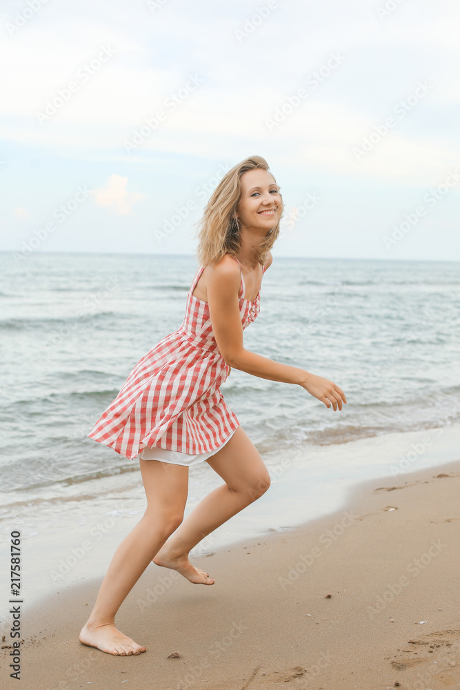 young woman is running along seashore, wearing short red checked dress young woman is running along seashore, wearing short red checked dress