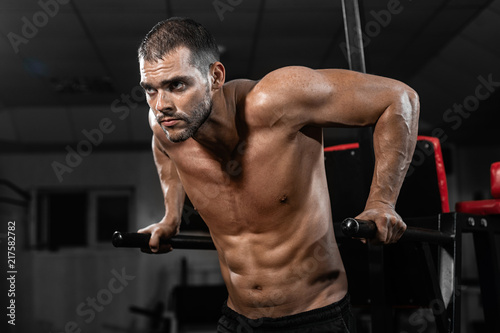 Muscular man doing push-ups on uneven bars in crossfit gym.