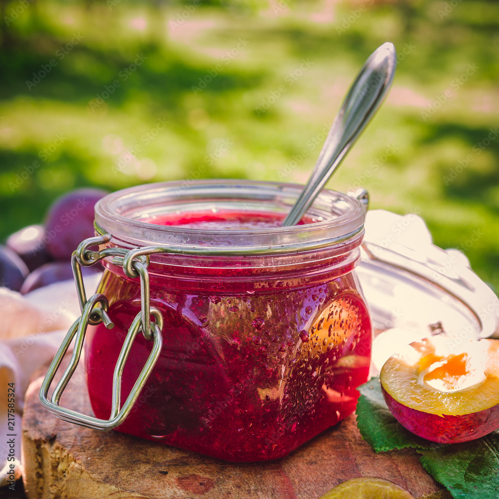 Glass jar with plum jam confiture and ripe plum berries in a basket on a wooden vintage table in the garden with a copy space, the idea of home canning and organic ecological bio nutrition Glass jar with plum jam confiture and ripe plum berries in a basket on a wooden vintage table in the garden with a copy space, the idea of home canning and organic ecological bio nutrition