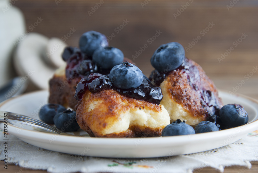 Homemade cheese donuts with berry jam and blueberry. Healthy breakfast or snack, round plate, rustic wooden background.