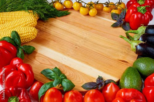 Food background with copy space for text. Fresh organic vegetables and herbs on the wooden table: bell pepper, corncobs, avocado, eggplants, cherry tomatoes, basil. Cooking concept