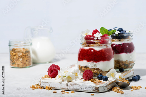desserts with granola, berry and fruit puree in jars on white table